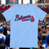 Light blue t-shirt with 'Believers' design in red and black text, worn by a person at a sports event.
